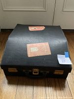 Closed black leatherette carrying case with stickers and brass latches