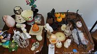 Various autumn and seasonal decor items arranged on a table including ceramic figurines, candle holders, glass votive holders, artificial flowers, and decorative pumpkins.