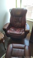 Front view of brown leather chair showing seat, backrest, armrests, and wood base with the ottoman positioned in front.