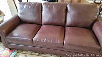Full front view of the brown leather sofa showing three seat cushions and back cushions with some wear.