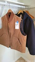 Brown Carhartt vest and navy blue coat hanging on wooden hangers in a closet