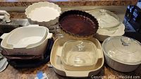 Set of CorningWare and glass baking dishes arranged on countertop, showing various sizes and shapes including covered dishes and pie pans.