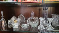 Shelf with crystal and cut glass items including candleholders, clocks, bell, and decorative pieces