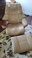 Full view of beige leather recliner with matching ottoman on floral rug