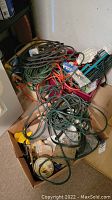 View of boxes containing green and orange extension cords, electrical outlets, wiring accessories and tape