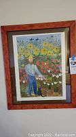 Framed signed print showing a farmer in a flower field with birds and cats