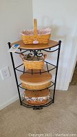 Four baskets displayed on black metal stand with wooden shelves against a wall.