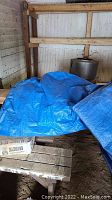 Two blue plastic tarps folded and placed on a wooden surface in a garage space, condition unknown.