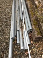 Multiple galvanized steel pipes of various lengths laid on gravel and against wooden beams