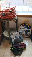 Photo of the lot showing coiled orange extension cords on the green round table, Orbit hose faucet timer with gloves in front, and tire chains in storage bag to right