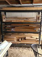 Front view of heavy metal shelving unit loaded with various lumber pieces and two wooden birdhouses on top shelf.