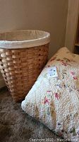 Woven laundry basket beside floral quilt on carpeted floor.