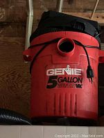 Close-up of a red Genie 5 gallon wet dry vacuum, showing branding and hose attachment details.
