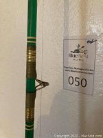 Close-up of green fishing pole body with brass fittings and line guide.