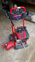 Full view of red Troy-Bilt pressure washer with engine, wheels, spray wand and red fuel container