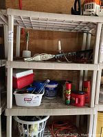 Front view showing four-level resin shelving unit with three ventilated shelves filled with various garage items (not included in sale).