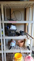 Plastic shelving unit containing assorted items such as black car buffers, sprayer, pot, and hand tools.
