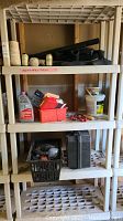 Plastic shelving unit with various items including vacuum attachments, tools, string, adhesive container, headphones, and Dewalt box