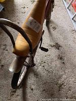 Close-up view of the sparkly gold banana seat with tall rusty metal sissy bar attached to the rear, showing dirt and wear on ground.