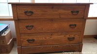 Front view of wooden dresser showing three drawers with original metal handles and wood grain finish.