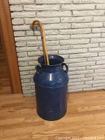 Full front view of blue metal milk can with one wooden cane inside