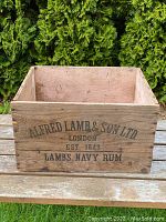 Front view of antique wooden rum crate showing 'ALFRED LAMB & SON LTD LONDON EST. 1849 LAMB'S NAVY RUM' stencilled in black paint on wood