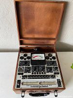 Open wooden case showing the electronic tube tester with multiple dials, switches, and analog meter.