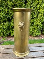 Front view of solid brass umbrella stand showing one lion's head handle with ring.
