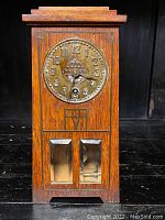 Front view of rectangular oak case clock with brass circular dial and stepped top