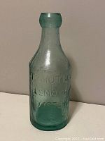 Front view of aqua glass bottle showing embossed text