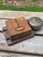 Wooden school bell ringer on a wooden surface showing iron bell and antique key on top.