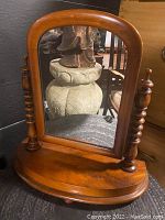 Front view of antique wooden vanity swivel mirror showing the curved rectangular mirror and turned spindle side columns.
