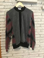 Front view of velour tracksuit top hanging on wooden hanger against brick wall.