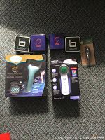 Photo of seven new electronic bathroom accessory items arranged on carpeted floor, all in original packaging.