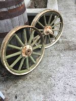 Pair of antique wagon wheels resting on ground, showing metal rims and green wooden spokes with rust and wear