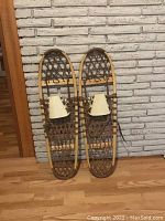 Pair of snowshoes upright against white brick wall, showing overall shape and condition