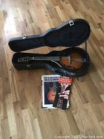 Mandolin in open hard case on wood floor with instruction books in front