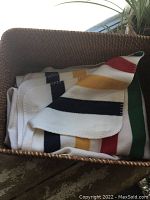 Folded vintage Hudson Bay blanket with distinctive multicolor stripes in a wicker basket.