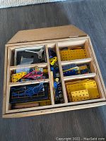 Wooden box with multiple compartments filled with various perforated metal plates and brackets in yellow, blue, and red colors.