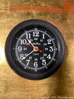 Front view of vintage Seth Thomas gauge style clock showing black textured bezel, black face, white and red hands, with 12 and 24 hour markers.