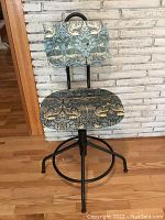 Front view of vintage swivel stool showing patterned fabric seat and backrest, metal legs, and circular footrest.