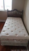 Full view of the bed showing the tufted mattress and floral box spring on the single size bedframe against wall near window.