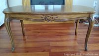 Front view of wooden coffee table with carved decorative apron and curved legs, placed on hardwood floor in front of fireplace.