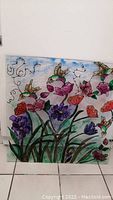 Front view of a square plexiglass artwork showing colorful hummingbird and floral design with visible outlines and painted elements.