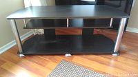 Full view of the black TV stand showing two shelves and chrome legs