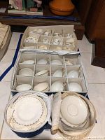 Full view of boxed set of demitasse cups and saucers along with small plates wrapped in paper in two separate boxes