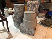 Several storage boxes stacked showing two rectangular and four round fabric-covered boxes in beige and blue toile fabrics