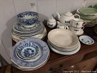 Stack of plates featuring blue and white floral designs with cups and Gilitzer German tea set on table