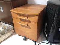 File cabinet front view showing two drawers with handles, wood grain laminate finish, mounted on casters.