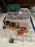 Overview of the lot including glassware, copper mugs, lobster mold, red covered Pyrex container, and ceramic mugs.